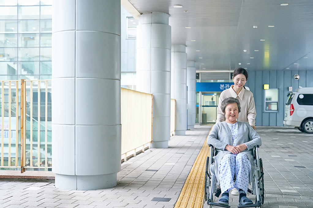 휠체어에 탄 사람을 뒤에서 밀어주는 사진