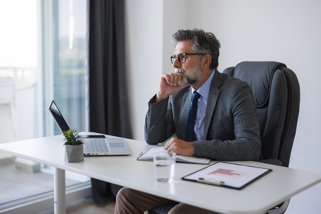 사무실 책상에서 노트북을 보며 생각에 잠긴 정장 차림의 남성