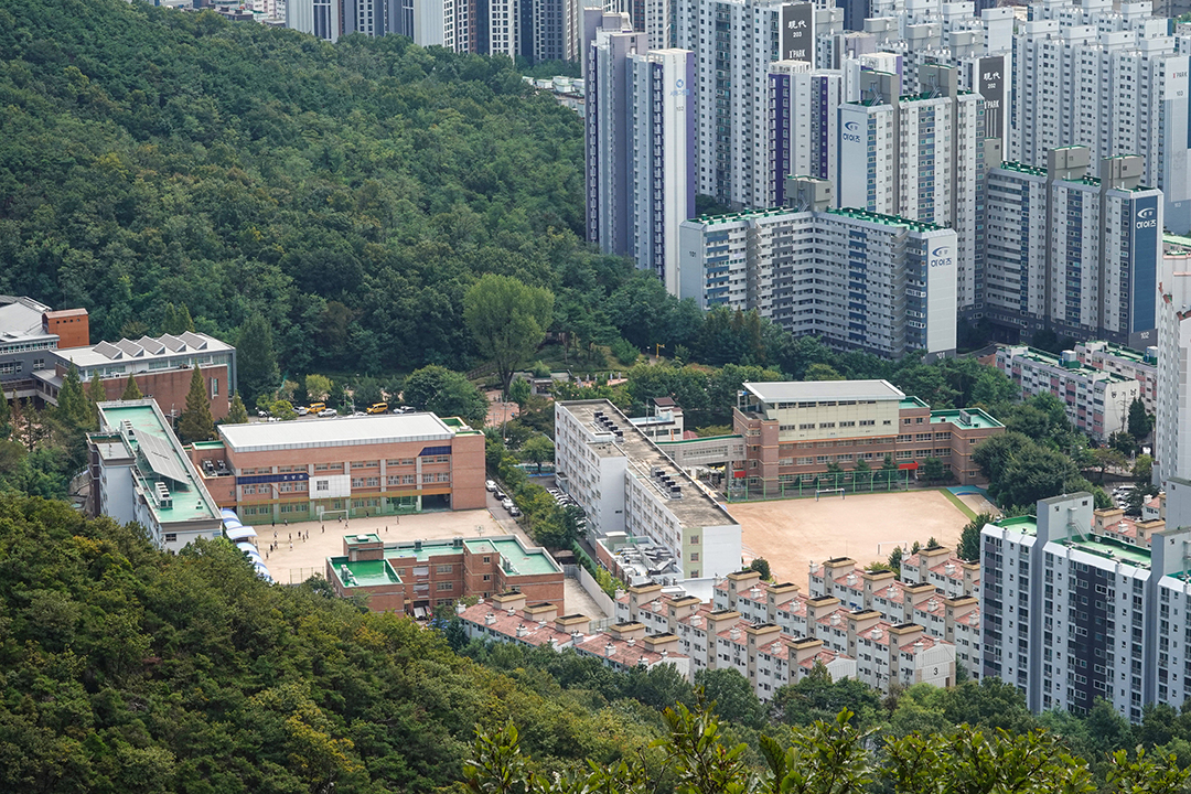산에 둘러쌓인 학교와 근처 아파트를 내려다 보는 전경 사진